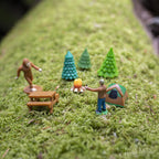 Experience a captivating miniature camping scene with the Bigfoot Basecamp, featuring soft vinyl figures set amidst tiny trees, a tent, campfire, and picnic table on a lush mossy surface—ideal for creating a distinctive desktop display.