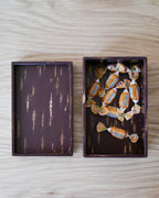 Open box with lid tray by Denshiro, one side containing small candies and the other empty.