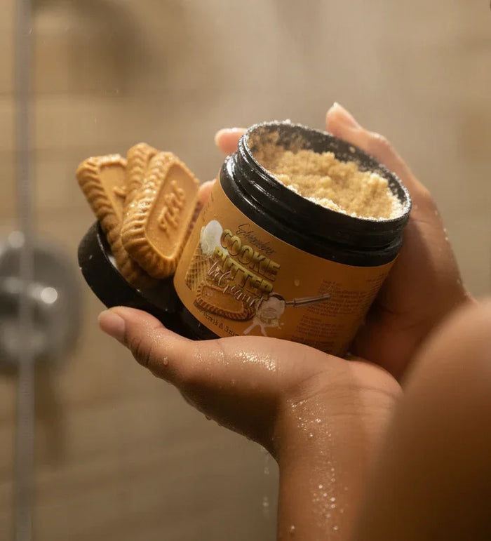 Person in shower holding jar of cookie butter body scrub with biscuit detail