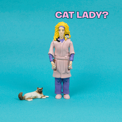Against a blue background, the Crazy Cat Lady® Action Figure stands beside a cat figurine, featuring a woman in a robe with six playful cats nestled in her hair and the text, "Crazy Cat Lady?