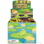 A box of vinyl toys called "Crowned Critters" showcases forest critters, featuring a frog donning a crown on lily pads. It comes with a warning label indicating small parts.