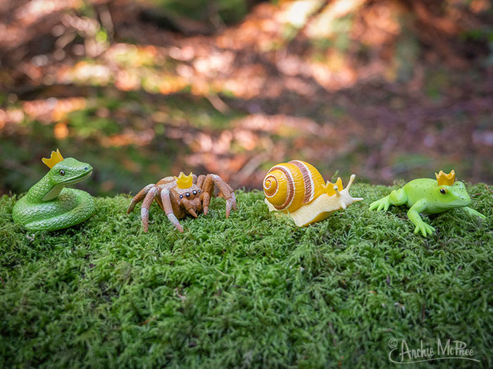 A mossy log in the forest hosts a collection of Crowned Critters—snake, spider, snail, and frog—each graced with regal crowns.