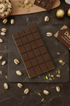 Dark chocolate bar with pistachios on black marble, surrounded by whole pistachios and chocolates