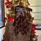 A person with their back turned to the camera showcases a black velvet hair bow clip with embellishments in their hair, with a decorated Christmas tree in the background.