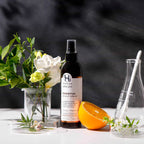 Essential scalp spray bottle with flowers and an orange on a dark background.