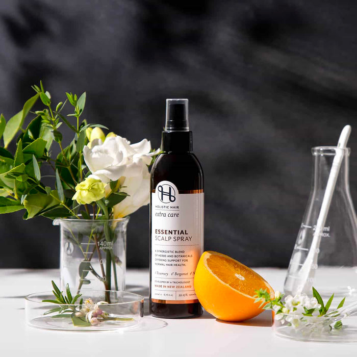 Essential scalp spray bottle with flowers and an orange on a dark background.