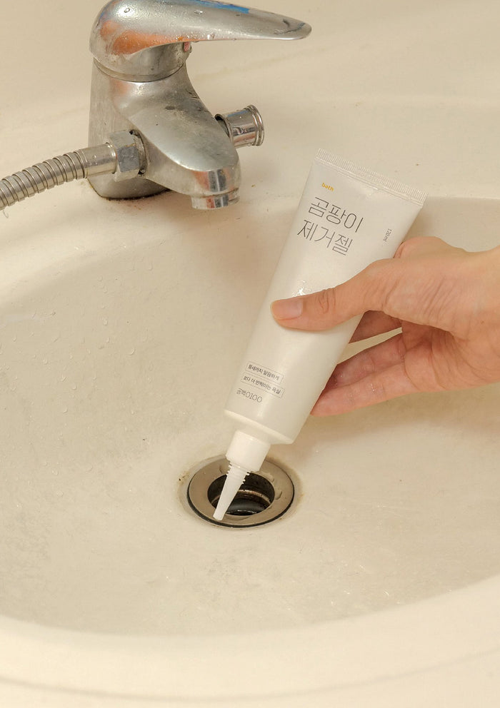 Hand using a tube of white cream to unclog a sink drain.