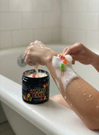 Woman using Gummy Bears body scrub in a bathtub, lathering aromatic exfoliant on arm