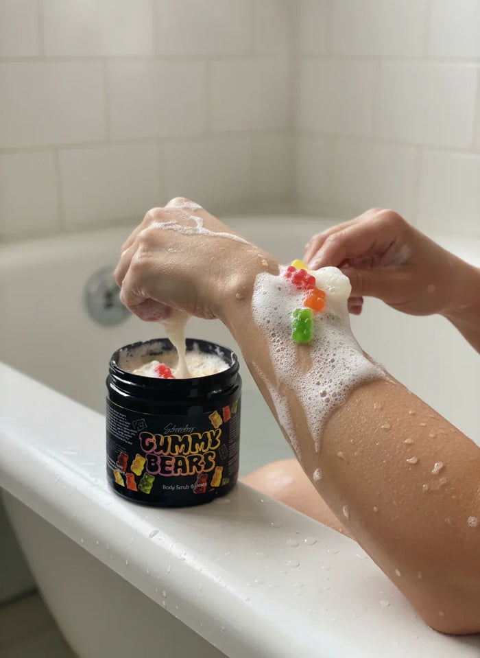 Woman using Gummy Bears body scrub in a bathtub, lathering aromatic exfoliant on arm