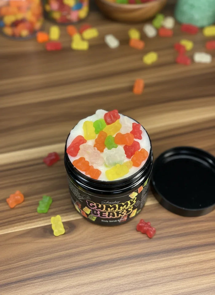 Overhead view of open jar of body scrub topped with colorful gummy bears on wooden surface