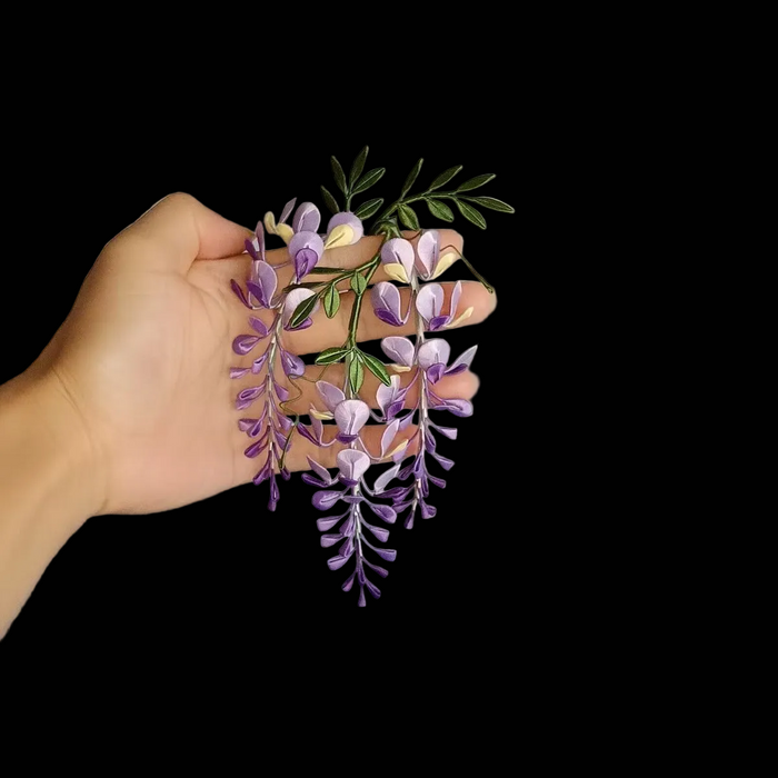 Handcrafted Chanhua wisteria decor cluster with purple gradient thread-wrapped flowers and green leaves held in a hand.