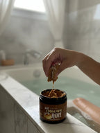 Hand using cinnamon roll body scrub by a bathtub with legs soaking in water