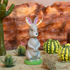 Discover the enchanting Jackalope Nodder, set in a desert scene complete with cacti and rugged rocks creating a breathtaking backdrop. Crafted from hard vinyl, this bunny figure merges mythical charm with an appealing design, embodying the essence of untamed frontier legends.