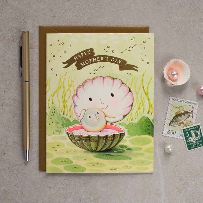 Mother's Day card with a shell and baby illustration, pen, and stamps on a gray surface