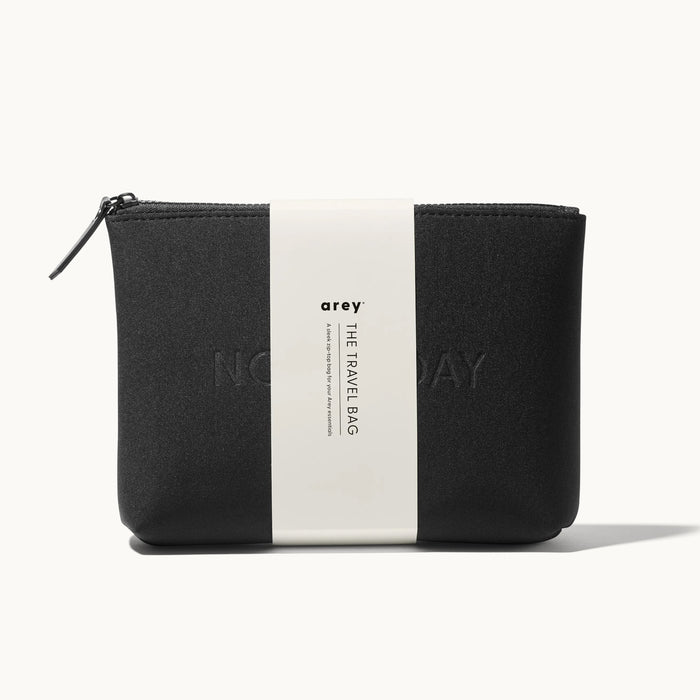 Arey "Not Today" black travel bag with a white paper band wrapped around it. The band reads: arey. THE TRAVEL BAG. A sleek zip-top bag for your Arey essentials.