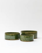 Silhouetted image of small, medium, and large ceramic oribe bowls with deep green glaze by Time and Style against white-gray background.