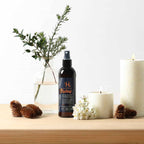 Bottle of hair styling product on a wooden surface with decorative elements like candles and plants.