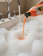 Pouring orange body wash into a foamy bubble bath under running water