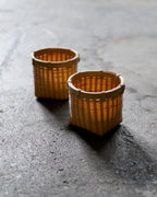 In situation image of two small round woven baskets by Kohchosai Kosuga on dark cement surface.