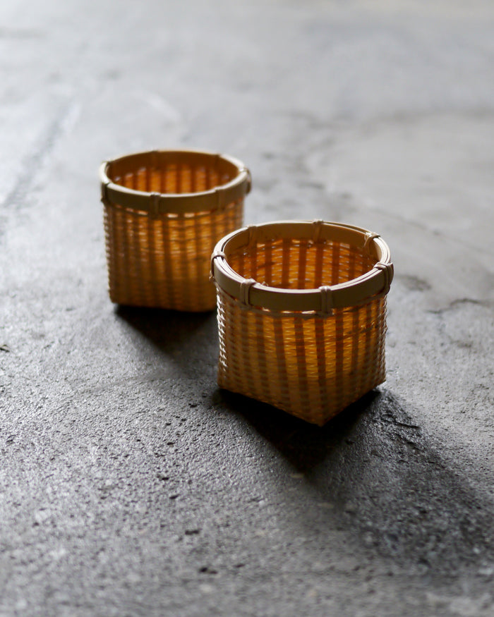 In situation image of two small round woven baskets by Kohchosai Kosuga on dark cement surface.