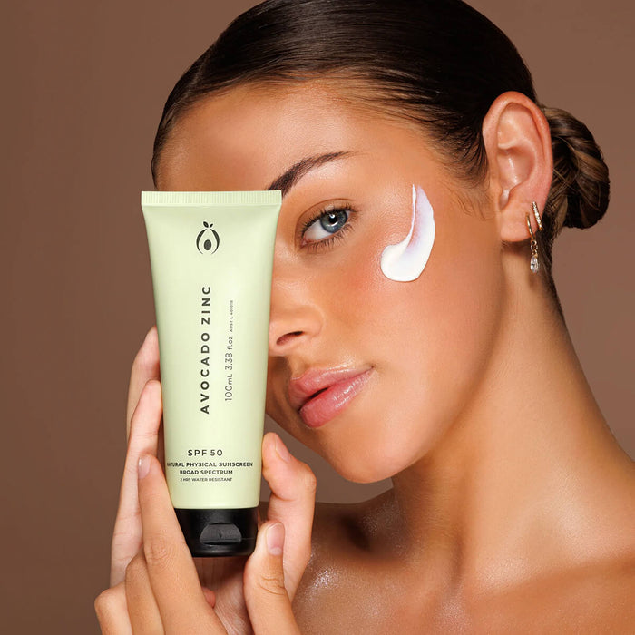 Woman applying sunscreen cream to her face with a tube of Avocado Zinc SPF50 Natural Physical Sunscreen.