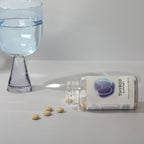 Infiniwell Thyroid Support supplement bottle on side with 60 tablets, spilled tablets and glass of water nearby