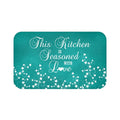 Teal chalkboard background with white vine scroll pattern across the bottom and the phrase "This Kitchen is Seasoned with Love" in white cursive script in the center.