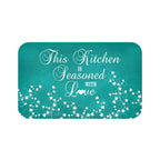 Teal chalkboard background with white vine scroll pattern across the bottom and the phrase "This Kitchen is Seasoned with Love" in white cursive script in the center.